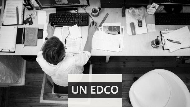 Black and white image of an employee working at a desk with papers and computer.