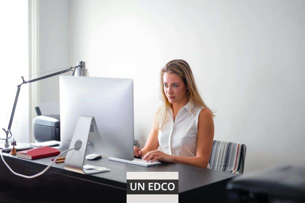 Blonde woman intensely working on a computer at her modern office workspace, featuring contemporary technology.